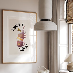 May include: A framed print with a whimsical illustration of stacked teacups and the text "Fancy a cuppa?" hanging on a light beige wall above a wooden dining table with woven chairs.