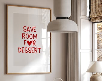 May include: A white framed poster with the text "SAVE ROOM FOR DESSERT" in red lettering with a red heart replacing the "O" in "FOR". The poster is hanging on a white wall above a white table with a marble top. Two wicker chairs are positioned on either side of the table. A white ceramic teapot and a white ceramic cup are on the table.