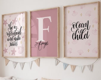 May include: Three framed prints with a pink background and black text. The first print says "Be a mermaid and make waves" with seashells and starfish. The second print has a large letter "F" with the name "Freyja" written below. The third print says "Ocean child" with seashells and stars.
