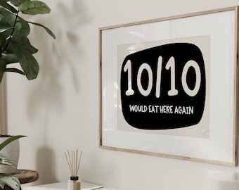 May include: A framed print with a black background and white text that reads "10/10 Would Eat Here Again". The print is hanging on a white wall above a white cabinet.