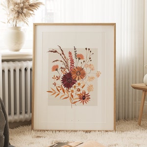May include: A framed print of a floral arrangement featuring dried flowers in shades of red, orange, and brown. The flowers are arranged in a bouquet and are set against a light beige background.