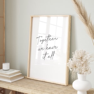 May include: A framed print with the text "Together we have it all" in black script. The print is displayed on a light wood bench with woven detailing, alongside a white vase with dried flowers and decorative baskets.