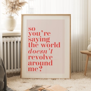 May include: A framed print with the text "so you're saying the world doesn't revolve around me?" in red on a pink background. The print is in a light wood frame, displayed in a room with a fluffy rug and a wooden side table.