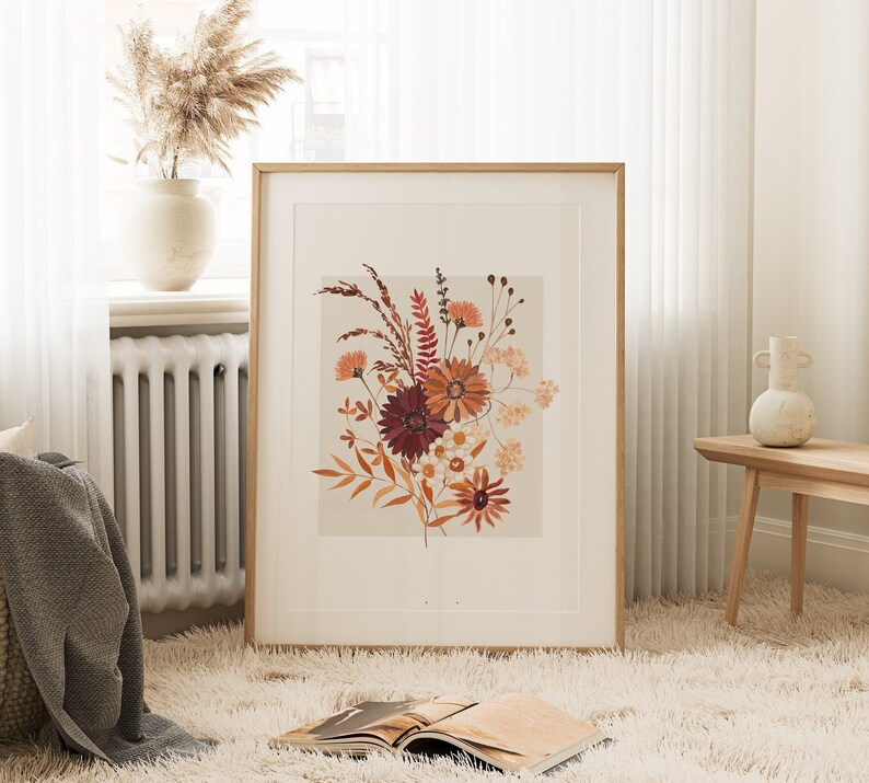 May include: A framed print of a floral arrangement featuring dried flowers in shades of red, orange, and brown. The flowers are arranged in a bouquet and are set against a light beige background.
