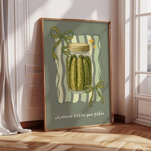 May include: A framed art print depicting a jar of pickles with a gold lid, set against a green backdrop with a striped design. The print includes green bows and the text "whatever tickles your pickle."