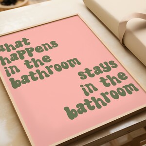 May include: A pink framed print with the text "What happens in the bathroom stays in the bathroom" in green letters.