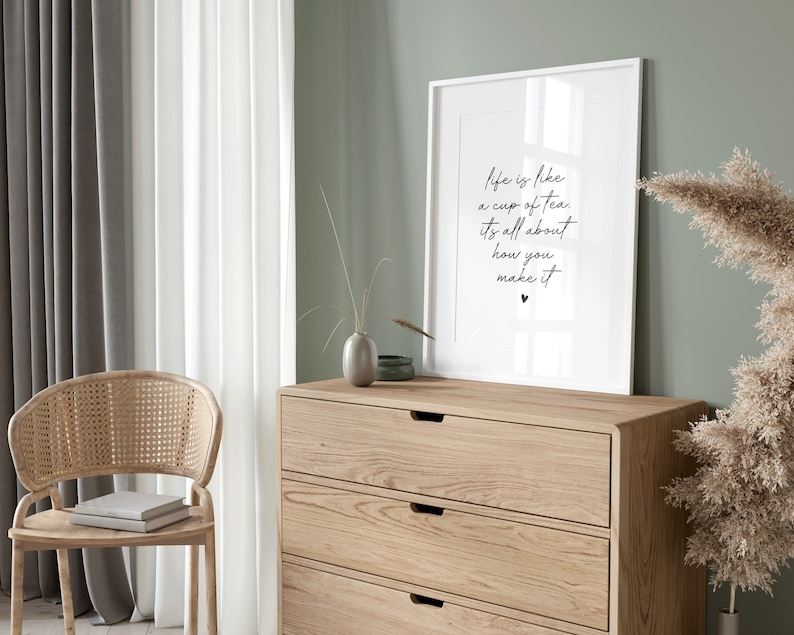 Puede incluir: Una impresi&oacute;n enmarcada con la cita "La vida es como una taza de t&eacute;, se trata de c&oacute;mo la preparas" en escritura negra sobre fondo blanco. La impresi&oacute;n est&aacute; colgada en una pared verde claro sobre una c&oacute;moda de madera con tres cajones.