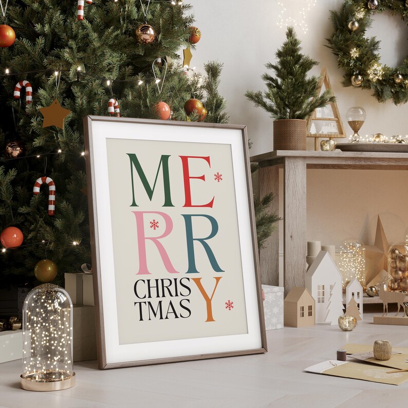 May include: A framed print with a beige background and the text "Merry Christmas" in colorful, stylized letters. The letters are in green, red, pink, blue, and orange.