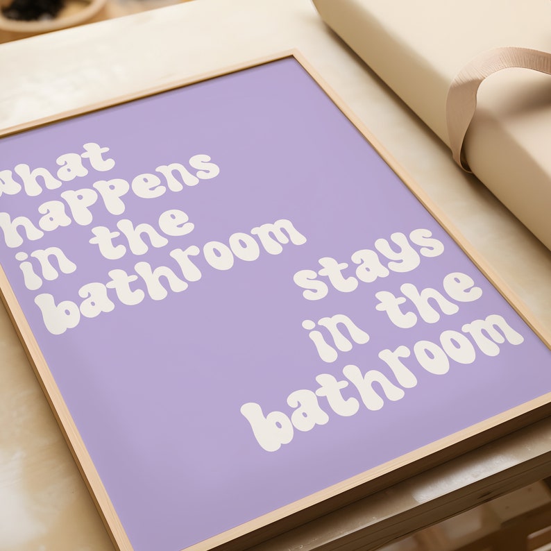 May include: A framed print with a light purple background and white text that reads "What happens in the bathroom stays in the bathroom".