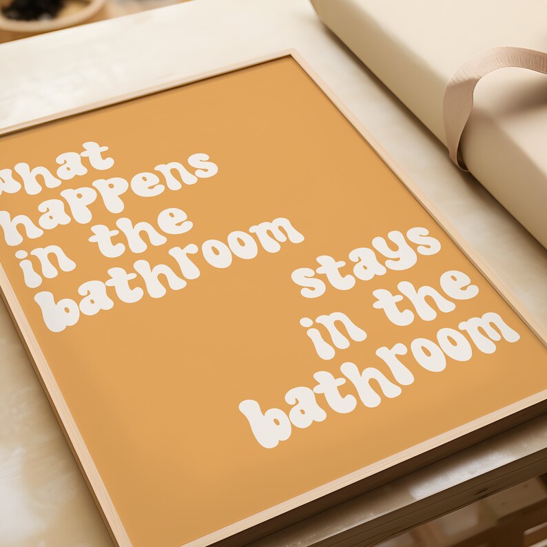 May include: A framed print with a yellow background and white text that reads "What happens in the bathroom stays in the bathroom".
