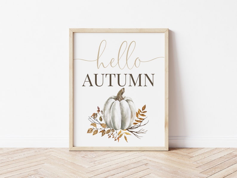 Puede incluir: Una impresi&oacute;n enmarcada con el texto "hello autumn" en una fuente cursiva. Una calabaza blanca con un tallo marr&oacute;n est&aacute; rodeada de hojas doradas y marrones.