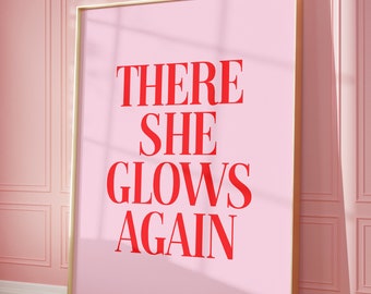 May include: A pink framed poster with the text "THERE SHE GLOWS AGAIN" in red letters.