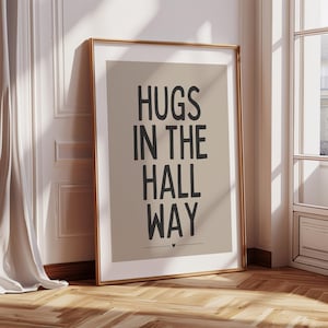 May include: A framed print with a beige background and black text that reads "Hugs in the hall way".