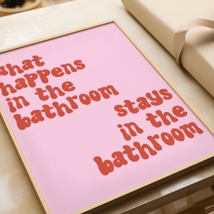 May include: A pink framed print with the text "What happens in the bathroom stays in the bathroom" in red.