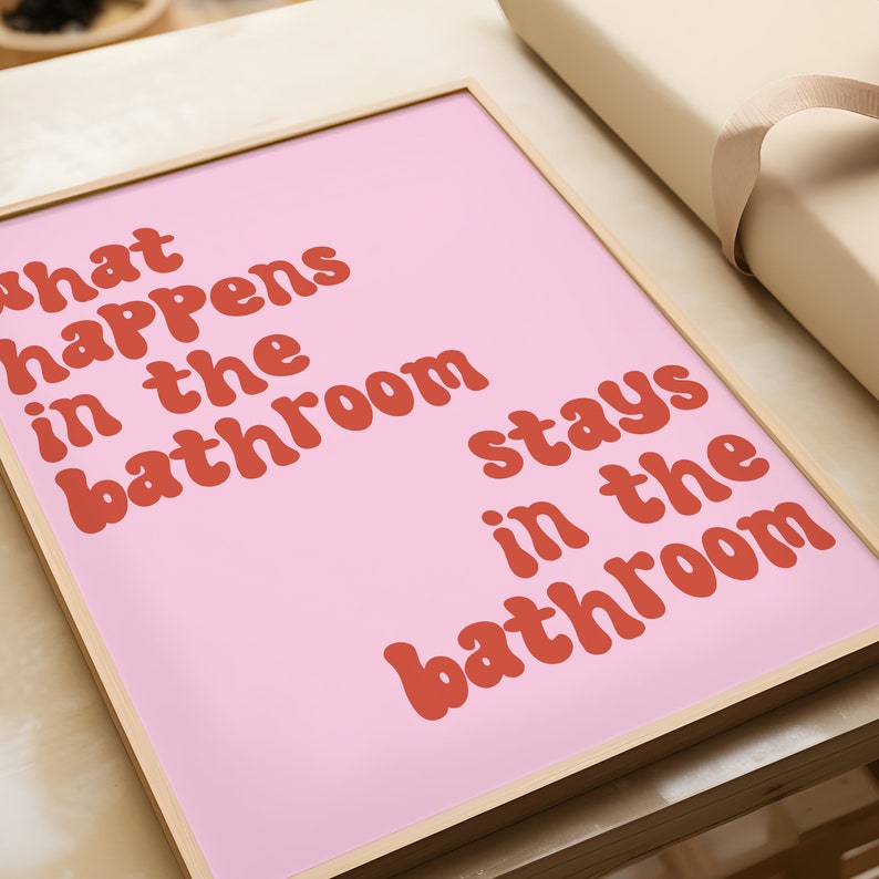 May include: A pink framed print with the text "What happens in the bathroom stays in the bathroom" in red.