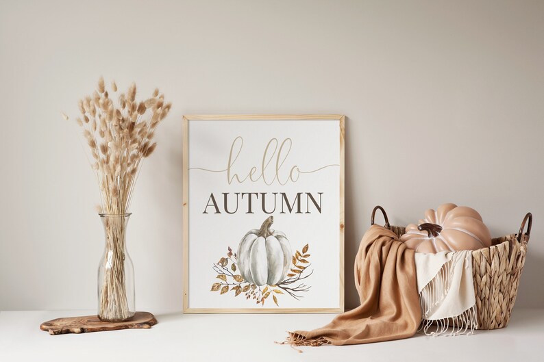 Puede incluir: Una impresi&oacute;n enmarcada con el texto "hello autumn" en una fuente cursiva. Una calabaza blanca con tallos marrones y hojas doradas se representa en el centro de la impresi&oacute;n.