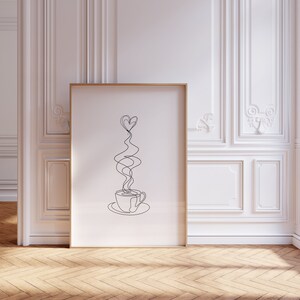 May include: A black and white line drawing of a coffee cup with steam rising in the shape of a heart. The drawing is framed in a gold frame and is hanging on a white wall.