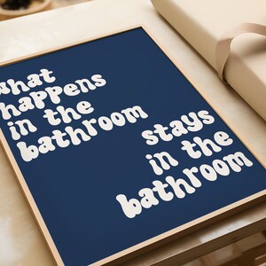 May include: A framed print with a navy blue background and white text that reads "What happens in the bathroom stays in the bathroom".