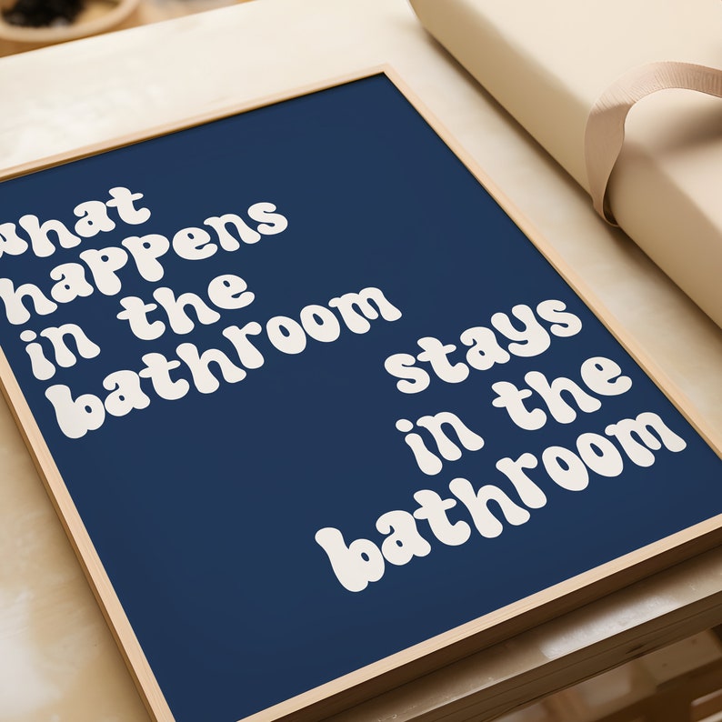 May include: A framed print with a navy blue background and white text that reads "What happens in the bathroom stays in the bathroom".