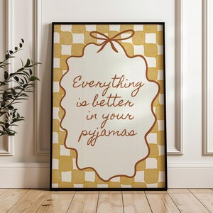 Może przedstawiać: Oprawiony wydruk z napisem "Everything is better in your pyjamas". Wydruk przedstawia kremowy wz&oacute;r z falistymi krawędziami i brązową kokardą na g&oacute;rze, na ż&oacute;łto-białym kratkowanym tle.