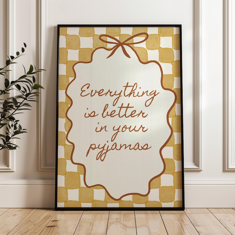 Może przedstawiać: Oprawiony wydruk z napisem "Everything is better in your pyjamas". Wydruk przedstawia kremowy wz&oacute;r z falistymi krawędziami i brązową kokardą na g&oacute;rze, na ż&oacute;łto-białym kratkowanym tle.