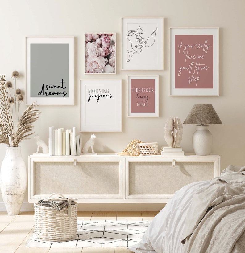 May include: A set of six framed prints with various designs and text. The prints are hung on a white wall above a white dresser with a white wicker basket and a white lamp. The prints feature a floral design, a line drawing of two faces, a gray background with the text "sweet dreams", a pink background with the text "if you really love me you'll let me sleep", a pink background with the text "this is our happy place", and a white background with the text "morning gorgeous".