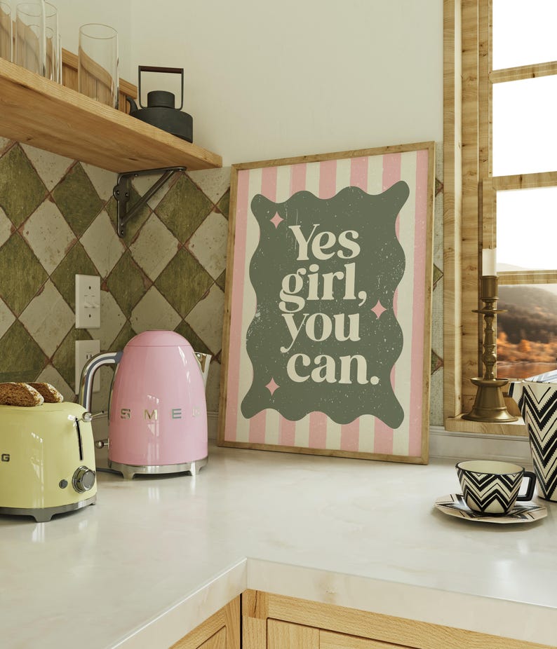 May include: A kitchen scene featuring a pink electric kettle and a yellow toaster. A framed print with the text "Yes girl, you can" is displayed. A cup and saucer with a black and white geometric design are also visible.