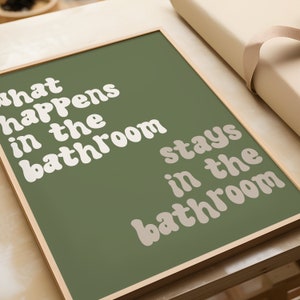 May include: A framed print with a green background and white text that reads "What happens in the bathroom stays in the bathroom".