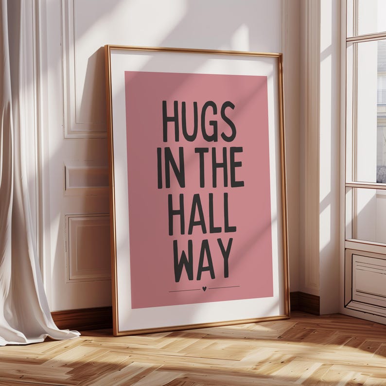 May include: A pink poster with a black frame and the text "HUGS IN THE HALL WAY" in black lettering.