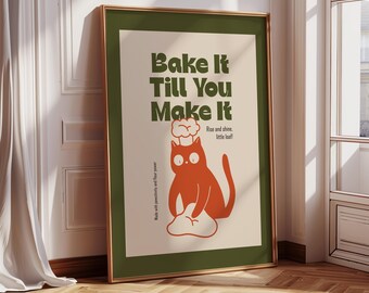 May include: A framed art print with a whimsical design. The print features a cartoon cat in orange, wearing a chef's hat, and baking on a cloud. The text reads "Bake It Till You Make It" in green, with additional text "Rise and shine, little loaf!"