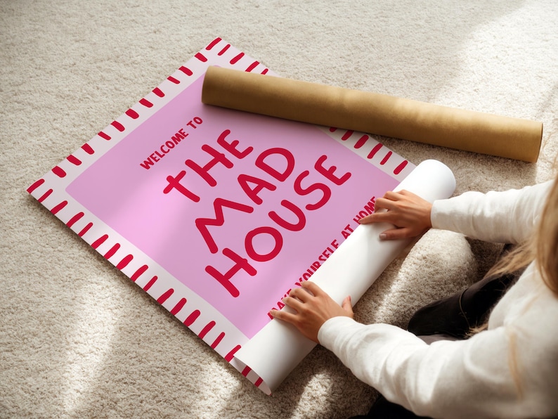 May include: A pink poster with the words "WELCOME TO THE MAD HOUSE" in red lettering. The poster is being unrolled, revealing the text "MAKE YOURSELF AT HOME". A brown cardboard tube is next to the poster.