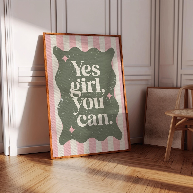 May include: A framed poster with the text "Yes girl, you can." The poster has a green, wavy-edged shape with white text on a pink and white striped background. The frame is brown.