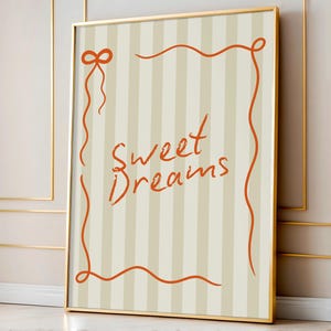 May include: A framed print with a beige and white striped background. The print features an orange ribbon border with the words "Sweet Dreams" written in orange cursive.
