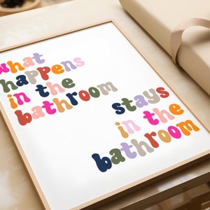 May include: A framed print with the text "What happens in the bathroom stays in the bathroom" in colorful, stylized letters.