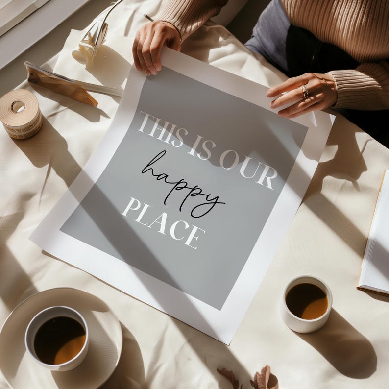 May include: A gray and white print with the text "This is our happy place" on a white surface with two cups of coffee.