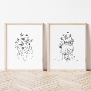 May include: Two black and white line art prints of a face with butterflies surrounding it. One print shows a face with hands covering the eyes, the other shows a face with hands covering the mouth.