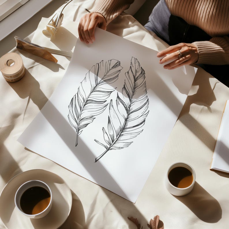 May include: A white sheet of paper with a black and white line drawing of three feathers. The paper is lying on a white surface with two cups of coffee.
