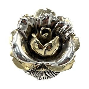 May include: A two-tone metal rose, featuring a combination of silver and gold hues. The flower's petals are intricately detailed, creating a realistic appearance. The rose is a decorative item, possibly a brooch or a pendant.