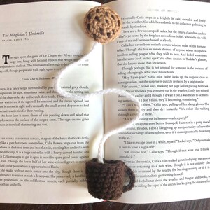 Puede incluir: Primer plano de un libro abierto con un marcap&aacute;ginas de galleta de crochet. El libro est&aacute; abierto en una p&aacute;gina con texto sobre una adivina y un circo. El texto dice "The Magician's Umbrella, Prague, March 1894".