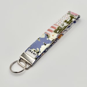 May include: A floral patterned key fob with a silver-colored metal clasp and key ring. The fabric features a patchwork design with blue, white, pink, and green floral patterns. The text "LIN & ALY COLLECTION" is printed on the fob.