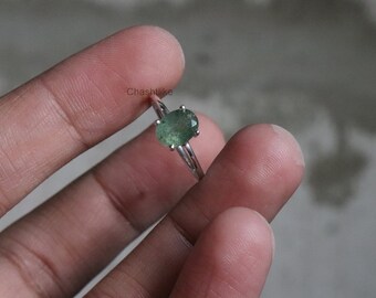 May include: A silver ring with a green oval gemstone. The ring is on a finger.