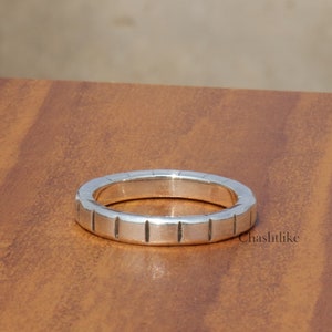 May include: A silver ring with a textured band. The band has a series of vertical lines.
