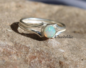 May include: A silver ring with a delicate design featuring a white opal gemstone. The ring has a double band and a simple, elegant style.