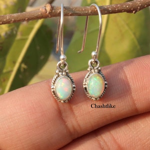 Könnte beinhalten: Ein Paar silberne Ohrhänger mit weißen Opal-Steinen. Die Ohrringe haben ein zartes Design und sind perfekt für den Alltag.