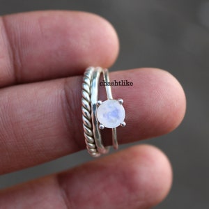 May include: A silver ring featuring a white moonstone set in the centre. The ring is stacked with two other silver bands.