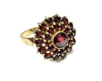 Puede incluir: Un anillo de oro con un gran granate rojo rodeado de granates rojos más pequeños.