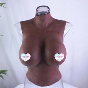 May include: A dark brown silicone breast form with a neck and shoulder piece. The form has two large breasts with heart-shaped stickers on each. The stickers have a heartbeat graphic and the text "GorgeousU".