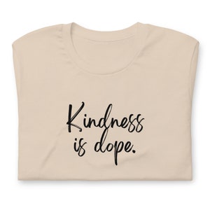 May include: A beige t-shirt with the text "Kindness is dope." printed in black.