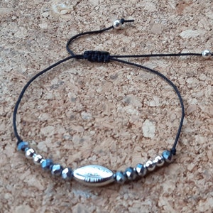 May include: Adjustable bracelet featuring a central silver-toned, oval bead flanked by faceted, gray beads and smaller silver beads. The bracelet is strung on a black cord with sliding knots and silver ball accents.