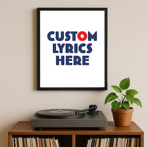 Puede incluir: Una impresión enmarcada con el texto "CUSTOM LYRICS HERE" en azul y rojo. La impresión está encima de un tocadiscos en un mueble de madera. Una pequeña planta en maceta está a la derecha del tocadiscos.